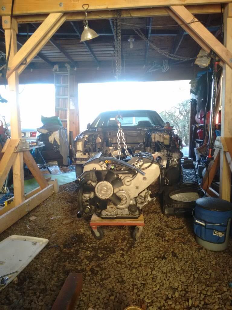 A photograph of removal of engine and transmission from an Audi A8 using a chain hoist and a wooden gantry